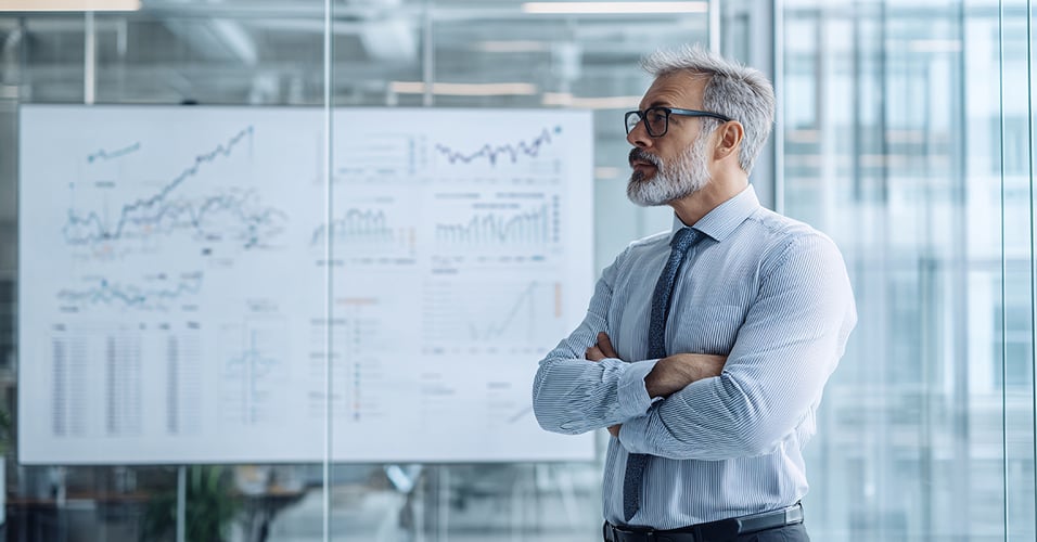 Man with crossed arms in front of whiteboard with charts