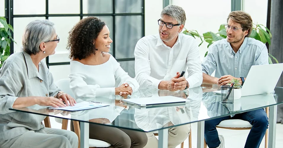 Several business professionals talking around a glass conference table